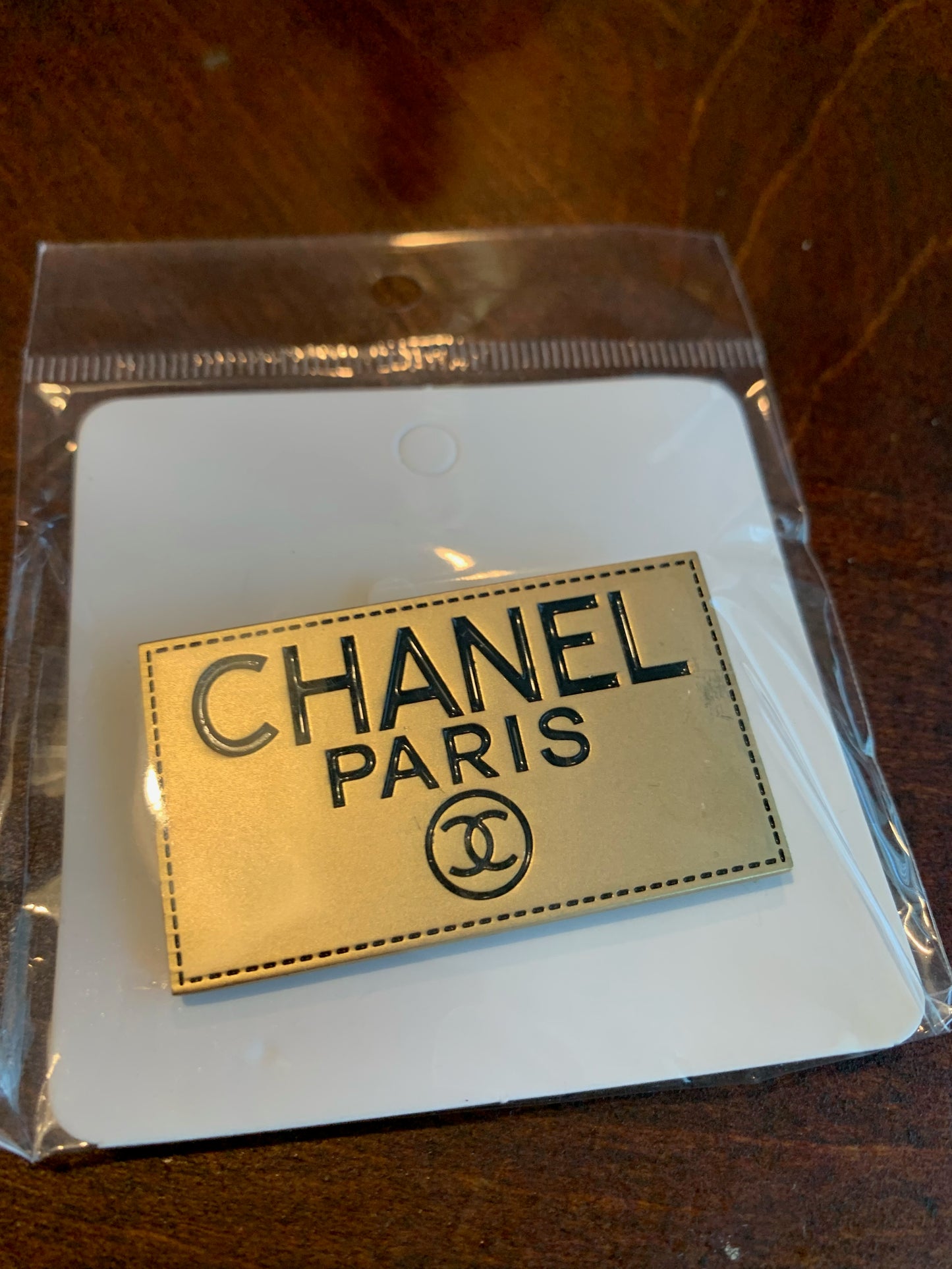 A Chanel Paris enamel pin with a gold-tone finish and black lettering, chanel inspired brooch designer inspired brooches