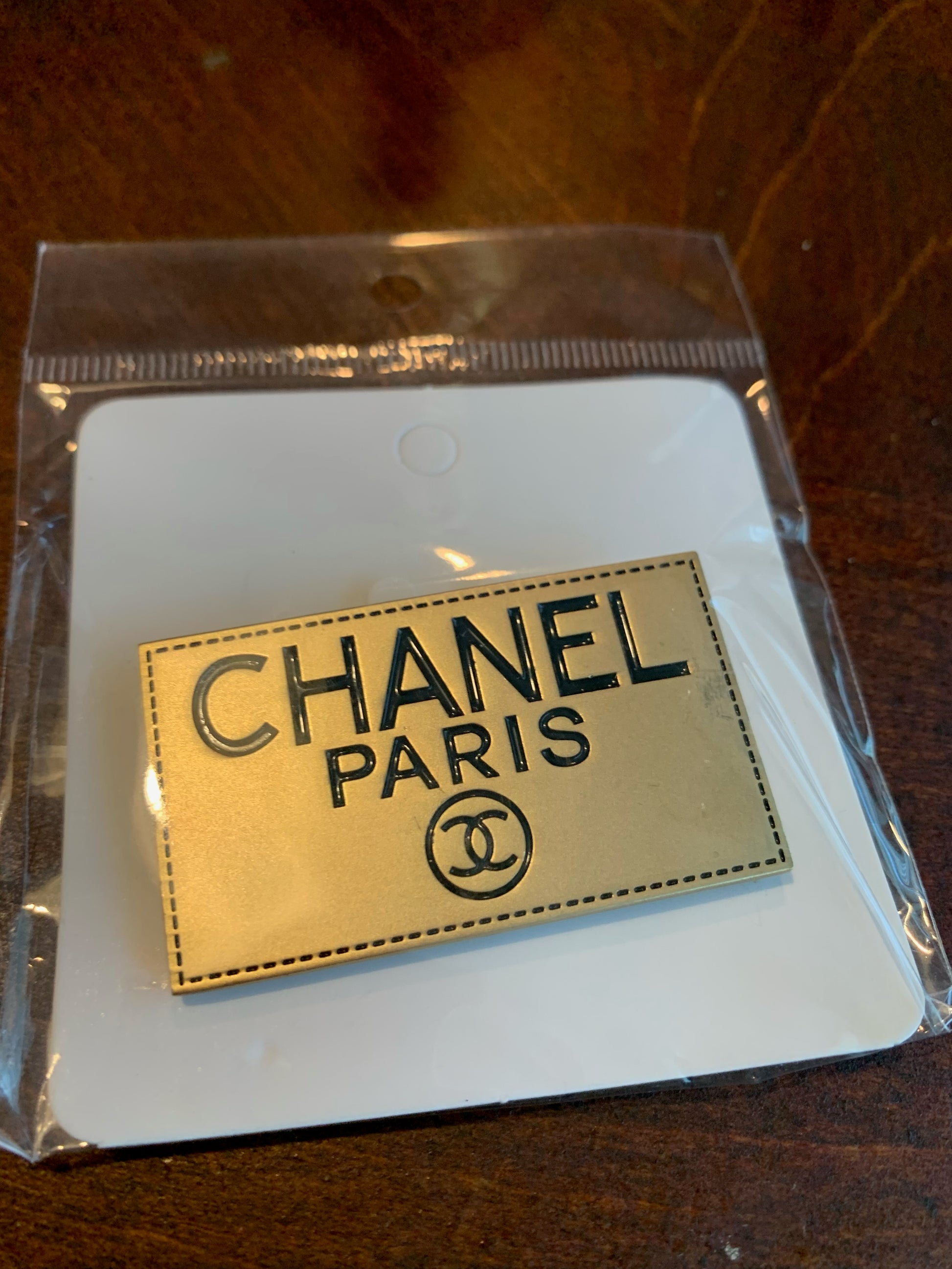 A Chanel Paris enamel pin with a gold-tone finish and black lettering, chanel inspired brooch designer inspired brooches