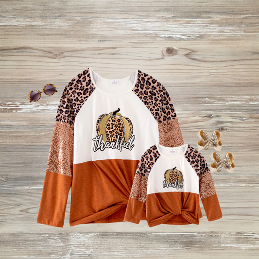 Matching “Thankful” mama and mini long-sleeve tops with leopard pumpkin graphic, sequin and leopard print sleeves, and rust-orange color block, perfect for fall and Thanksgiving family outfits.