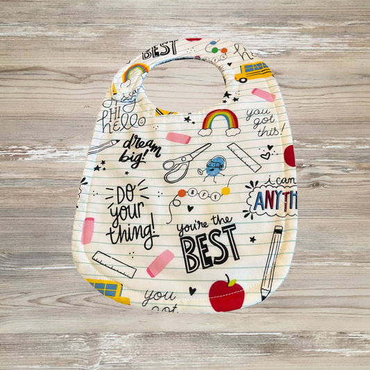 Back-to-school adaptive bib with positive doodles for kids with special needs or drooling, featuring rainbows, pencils, apples, rulers, and uplifting phrases on lined paper background. bib with motivational phrases