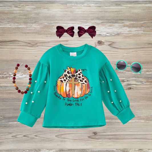 Teal girls' long sleeve top with pumpkin and cross graphic, leopard-print bow, pearl sleeve detail, and Psalm 136:1 scripture. Girl's boutique fashion top for holidays, thanksgiving, christian clothing give thanks to the lord