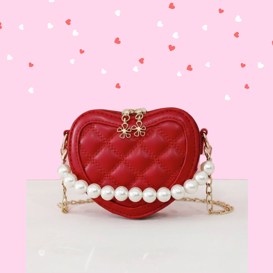 A red heart-shaped kids' handbag with a quilted pattern and a decorative white pearl handle. girl's heart shaped purse for valentine's online boutique handbags and purses for babies and kids red heart purse, girl's crossbody purse, purses and handbags for toddler girls, girl's vegan leather purses, vegan leather handbag kids