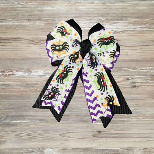 Halloween-themed decorative bow with spider design Girls Halloween hair bow with smiling spider and spider web design, purple chevron pattern, and black ribbon trim Girls Halloween boutique bow